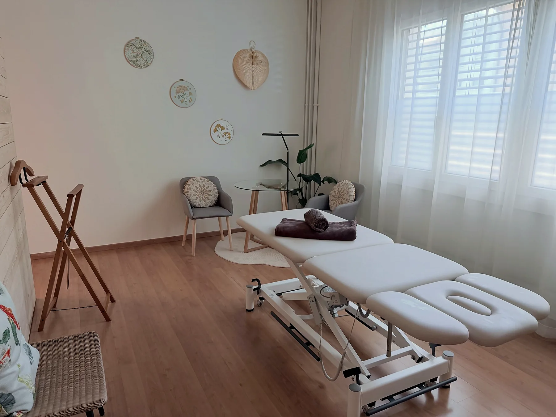 Heller Behandlungsraum mit Massageliege, Sesseln und Tageslicht